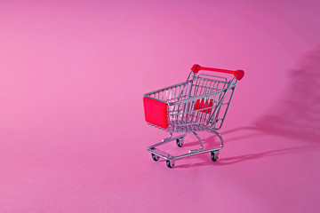 red trolley shopping chart on pink background with lots of empty copy space. concept of sales and online shopping