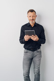 Relaxed man in jeans standing holding a tablet