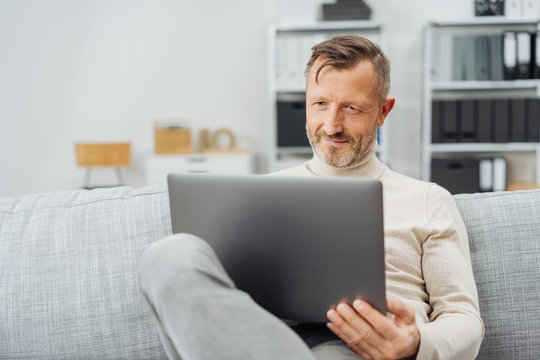 Man sitting using a laptop with a pleased smile