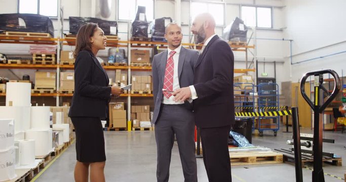 4K Businesswoman meeting with business associates in factory warehouse, looking at computer tablet & discussing inventory. Slow motion.