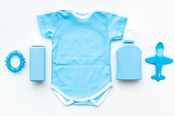 Blue baby clothes for little boy. Bodysuit, toys, cosmetics on white background top view