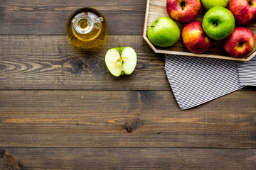 Light salad dressing. Apple cider vinegar in bottle among fresh apples on dark wooden background top view copy space