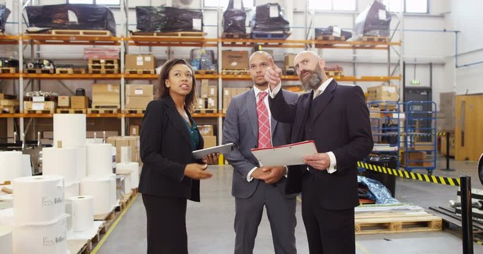 4K Businesswoman meeting with business associates in factory warehouse, looking at computer tablet & discussing inventory. Slow motion.