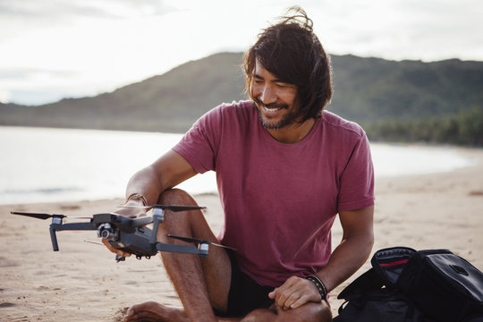 Man holding drone while sitting at beach against sky