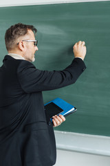Male teacher writing on a blank chalkboard
