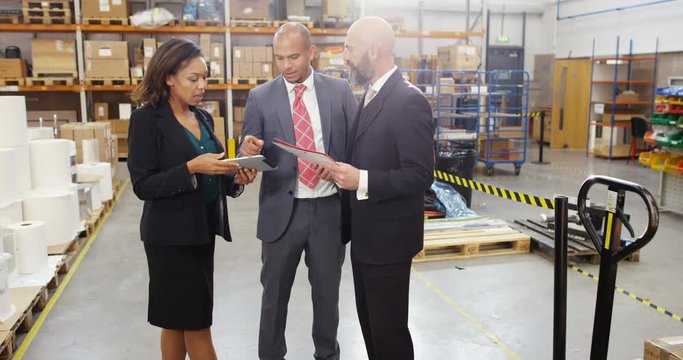 4K Businesswoman negotiating a deal with investors in factory warehouse, looking at computer tablet & discussing inventory. Slow motion.
