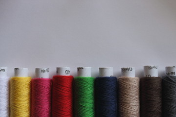 Spools of colorful threads on white background with copy space. Line of cotton threads. Needlework and sewing concept. Sewing and embroidery hobby background. 