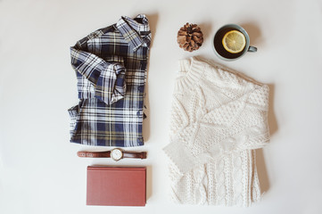 woman casual fashion set flat lay. Plaid shirt, knitted sweater, watch and book on white background. Stylish outfit top view.