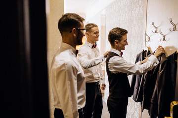 stylish groom laughing and having fun with groomsmen while getting ready in the morning for wedding...