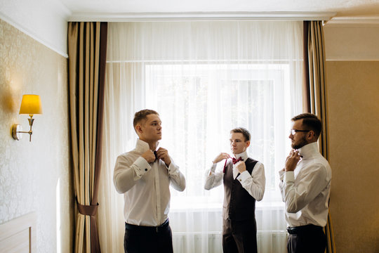 stylish groomsmen helping happy groom getting ready in the morning for wedding ceremony.