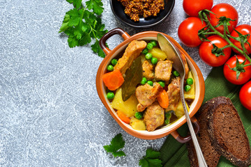 Roast with pork, potatoes, carrots and green peas on a concrete background.