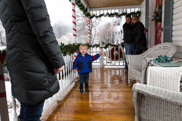 Three Adults And One Child Greet One Another On A Christmas Decorated Front Porch For The Holidays