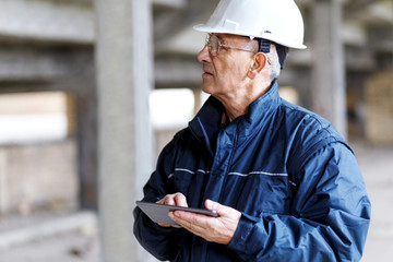 Senior construction manager controlling building site using digital tablet.