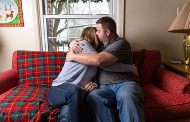 A Young Caucasian Couple Excitedly Waits And Prays For Good News As They Sit On Their Living Room Couch.