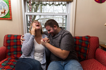 A Young Caucasian Couple Excitedly Waits And Prays For Good News As They Sit On Their Living Room Couch.