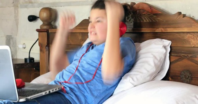 School boy with headphone using laptop computer on the bed
