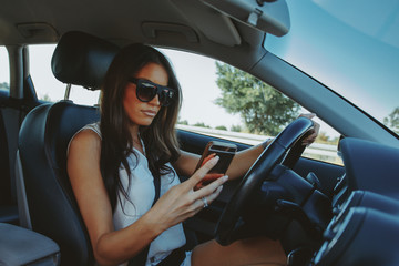Fototapeta na wymiar Attractive brunette drives a car and typing message on phone