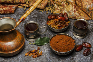 Turkish coffee in silver dishes with ground coffee raisins and dates on a marble background.