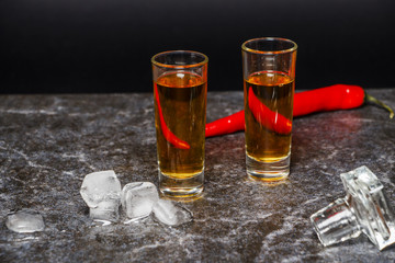 A glass of cognac or whiskey with red pepper on the background of marble.