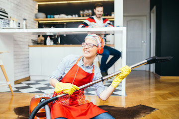 Beautiful young smiling woman listening to music while cleaning house with vacuum cleaner.