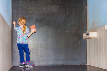 Cute little girl writing on empty chalkboard