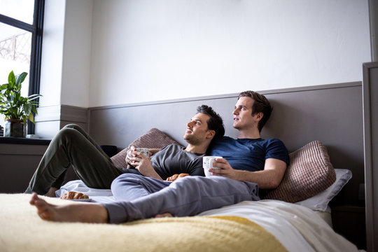 Young male couple relaxing with coffee in bed
