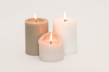 Set of three burning candles against a white background