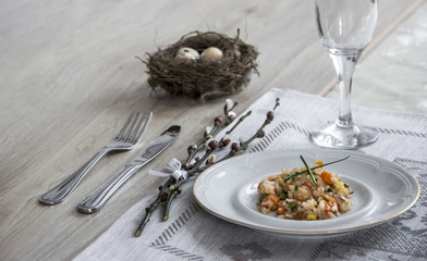 on a table a napkin with a plate of vegetable stew a glass of fork and a branch of a willow's nest with quail eggs 