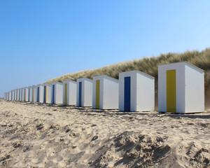 Fototapeta na wymiar A row of identical beach huts on a sandy beach at Cadzand Bad in Zeeuws-Vlaanderen in the far south west of the Netherlands.