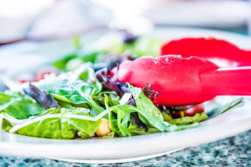 Macro closeup of caesar salad on plate with red tongs, parmesan cheese, dressing and tongs