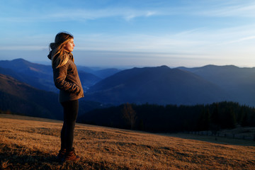 Shot of a young woman looking at the landscape while hiking in the mountains. Happy traveler standing on top of a mountain and enjoying sunset view