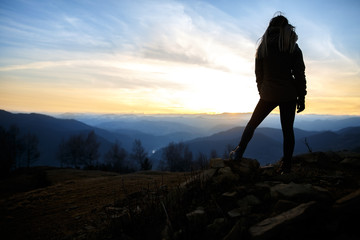 Happy young blonde woman portrait. Beauty in Nature. Young woman hiker hiking on mountain trail. Travel concept. Happy traveler standing on top of a mountain and enjoying sunset view