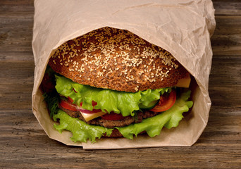 Large hamburger on a wooden table is packed in a paper bag