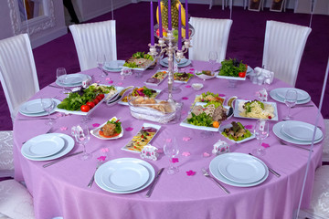 Wedding table decorated with candles, served with cutlery and crockery and covered with a tablecloth . Salad . Pink tablecloth . White chairs . White wedding table. A table decorated with balloons.