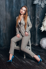 A beautiful girl in a gray suit is sitting on a chair in a Christmas decor.