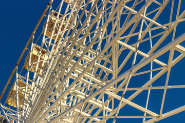 Metal white frame of a ferris wheel on a blue sky background. Abstractive fragment of architecture.