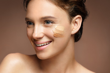 Beautiful woman with tone cream lines on her face. Photo of smiling brunette woman with perfect makeup on brown background. Skin care concept