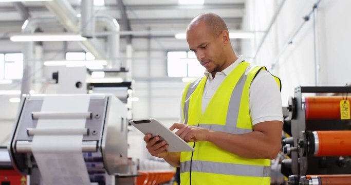 4K Business manager in a printing factory looking down at computer tablet with machinery in background