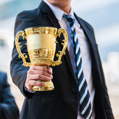 Unidentified business people holding the golden trophy cup for their success winner in business project.  The best business man has achieved their desired gold with golden trophy in middle city town.