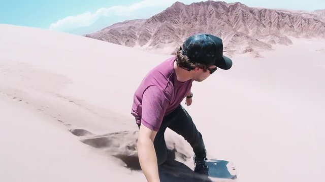 Young man sandboarding over great Sand Dunes of the Dead Valley, Atacama desert. Man using an action camera when slide on a sandboard.	