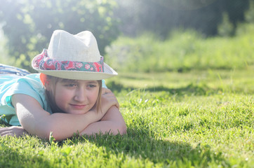 A girl resting on the lawn in a summer sunny day. The teenager in a hat dreams.