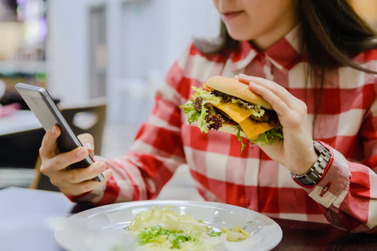 woman eat humburger while searfing the phone