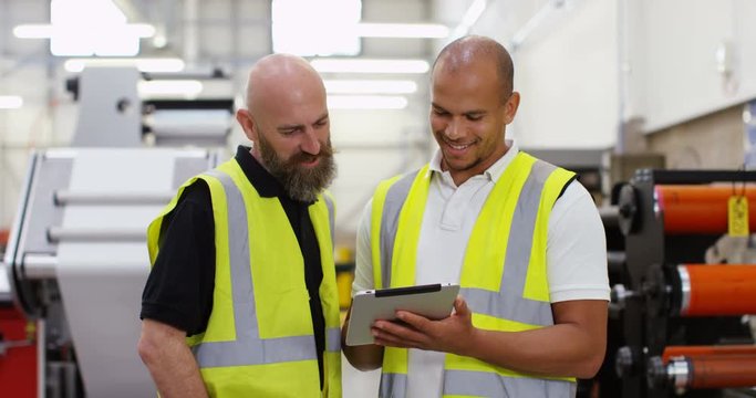 4K Cheerful coworkers in a printing factory looking down at computer tablet, with machinery in background
