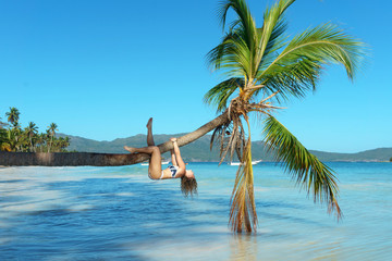 young girl in bikini climbs on a palm tree upside down. Exotic Vacation concept