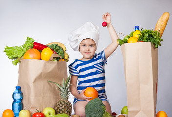Little happy girl in the hat of the chef with big bags products holding a radish. A variety of...
