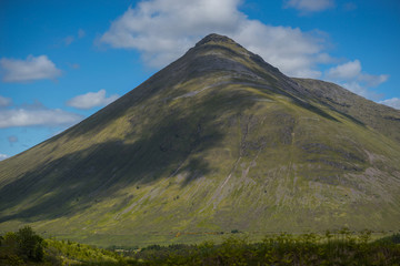 Naklejka premium Mountain landscape in the Glencoe area in Scotland, Springtime view mountains with grassland and countryside road in the valley of the Scottish highland near Glencoe