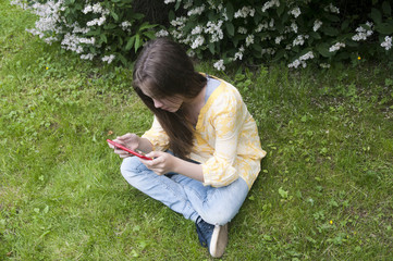 Fototapeta premium Beautiful teenager girl with tablet computer sits on the grass in Park. Photo