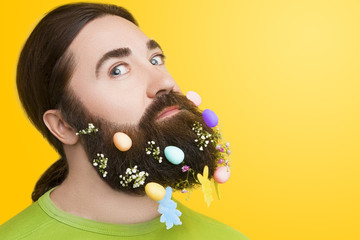 Happy Easter concept. Male man with beard with spring flowers and easter eggs on yellow isolated background