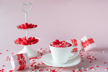 Festive background.  Coffee cup, white two tier serving tray full of multicolor sweet sprinkles sugar candy hearts and packing Valentine's  Day gifts  Love and Valentine's day concept.