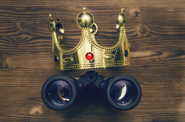 VIP premium search. Binoculars and golden crown on wooden desk table background. In searhing for something special.